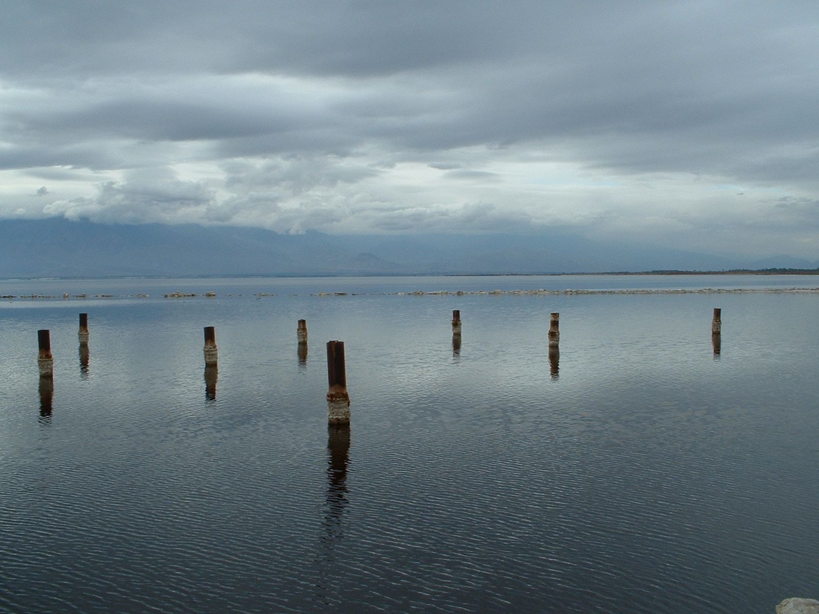 Still dark water and a line of wooden posts beneath a stormy sky